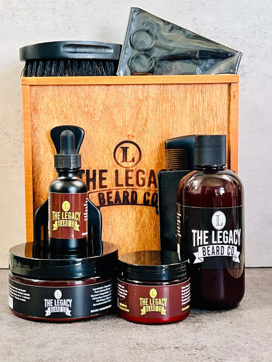 Beard kit with a white background on a concrete surface. This Kit includes:8 oz. Beard Wash, 8 oz., Beard Conditioner, 3 oz. Beard Enhancer, 1 oz. Beard Oil, scissors, beard brush, wooden comb, Wood keepsake box
