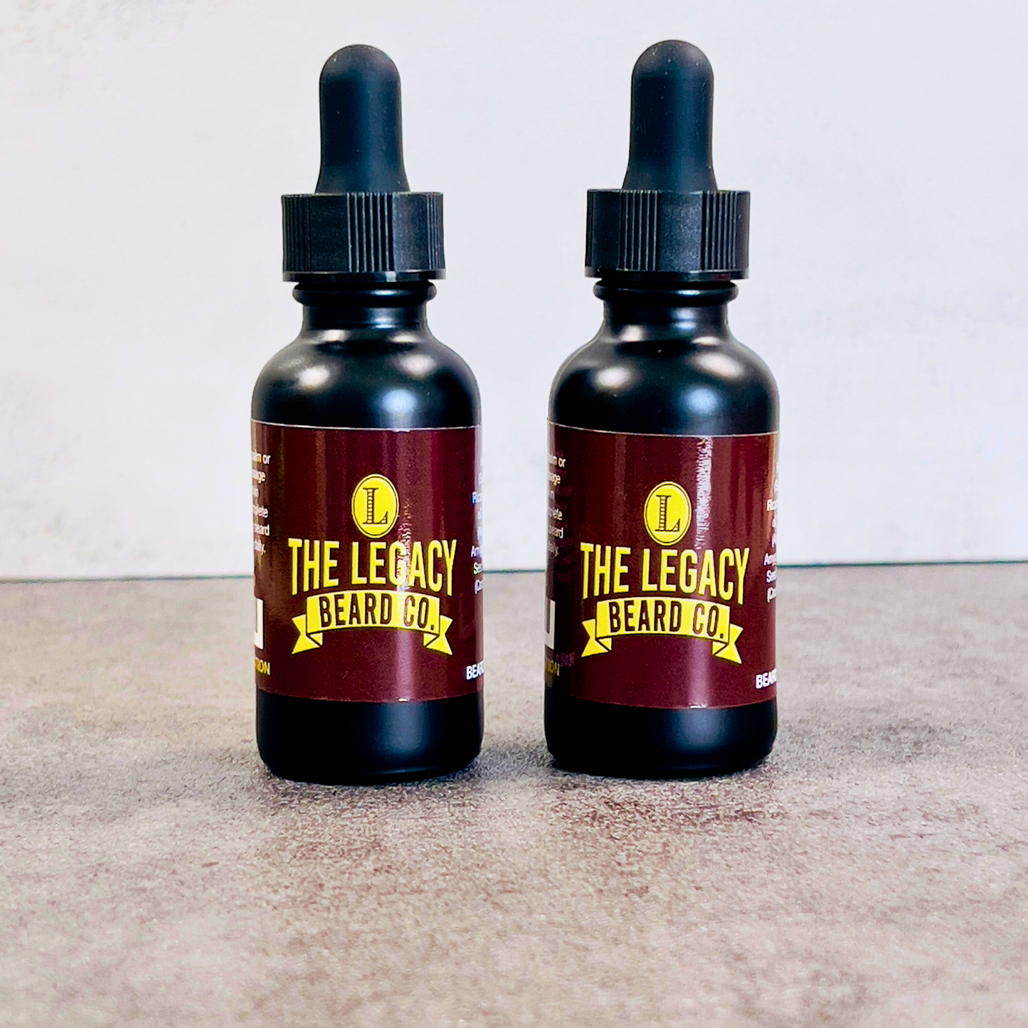 Two black bottles of beard oil with dropper caps, labeled 'THE LEGACY BEARD CO.', one with 'WHISKEY' and the other with 'BOURBON' scent profiles.
