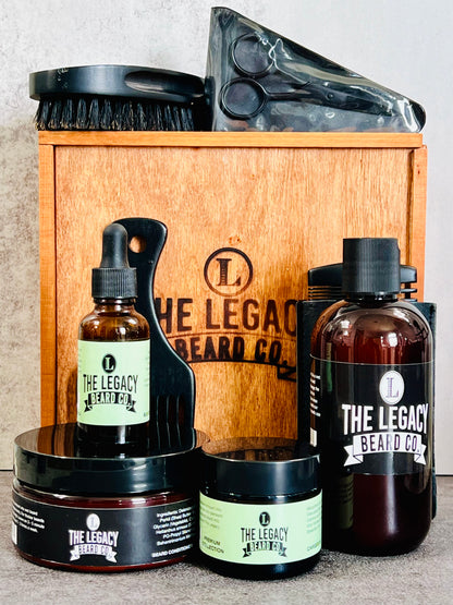 A grooming kit for beard care containing bottles of beard wash, conditioner, and oil, along with a beard butter container, wooden comb, boar bristle brush, beard pick, and stainless steel scissors, all displayed in front of a wooden box with the brand logo.