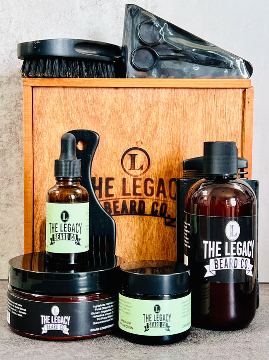 A grooming kit for beard care containing bottles of beard wash, conditioner, and oil, along with a beard butter container, wooden comb, boar bristle brush, beard pick, and stainless steel scissors, all displayed in front of a wooden box with the brand logo.